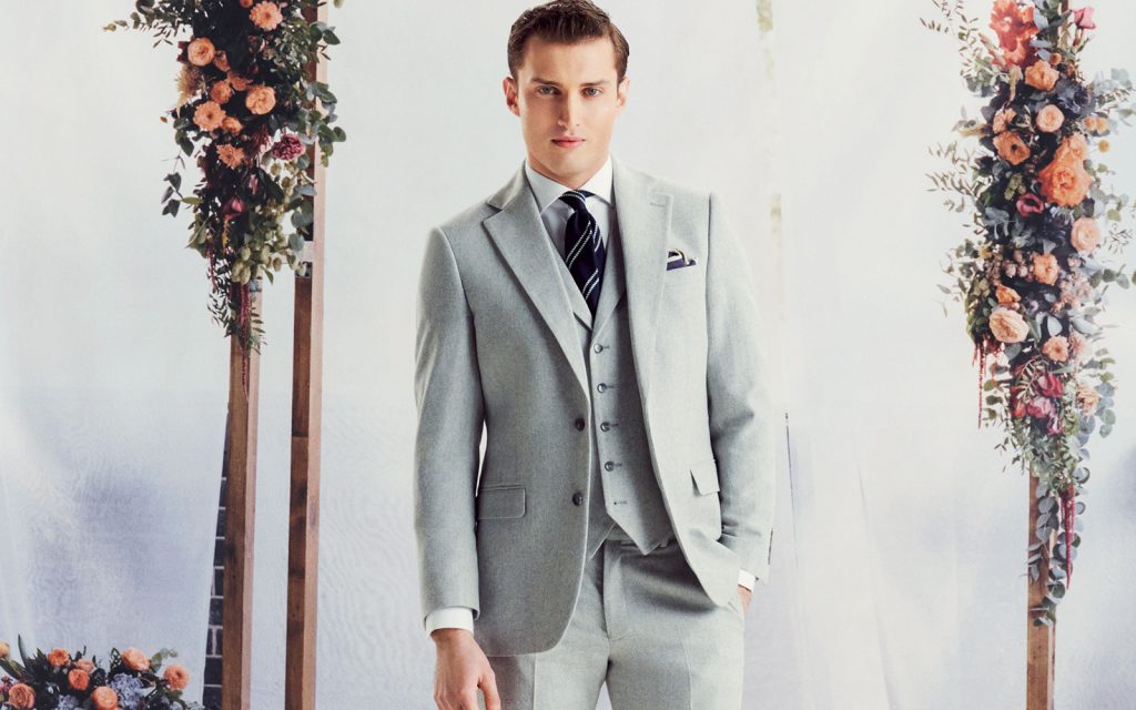 how to style a men's waistcoat; man at wedding in three piece grey suit looks at the camera 
