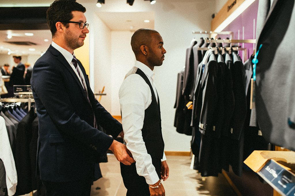 Moss Bros tailor fitting a man's black waistcoat.