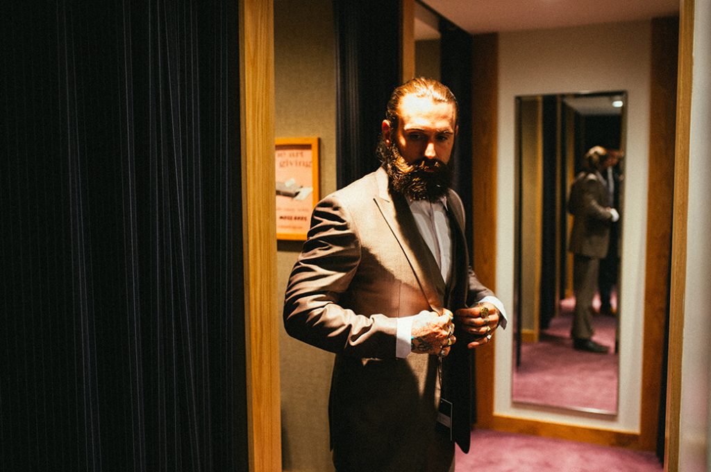 Bearded man trying on a suit to buy in the mirror.