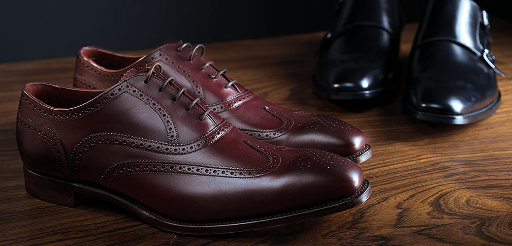 A pair of polished brown leather shoes on a wooden table.