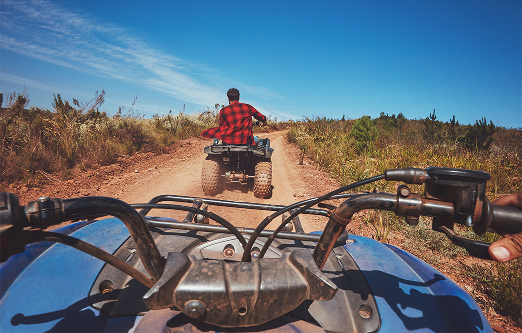 Two men on quadbikes driving along a dirt track on a summer stag do. 