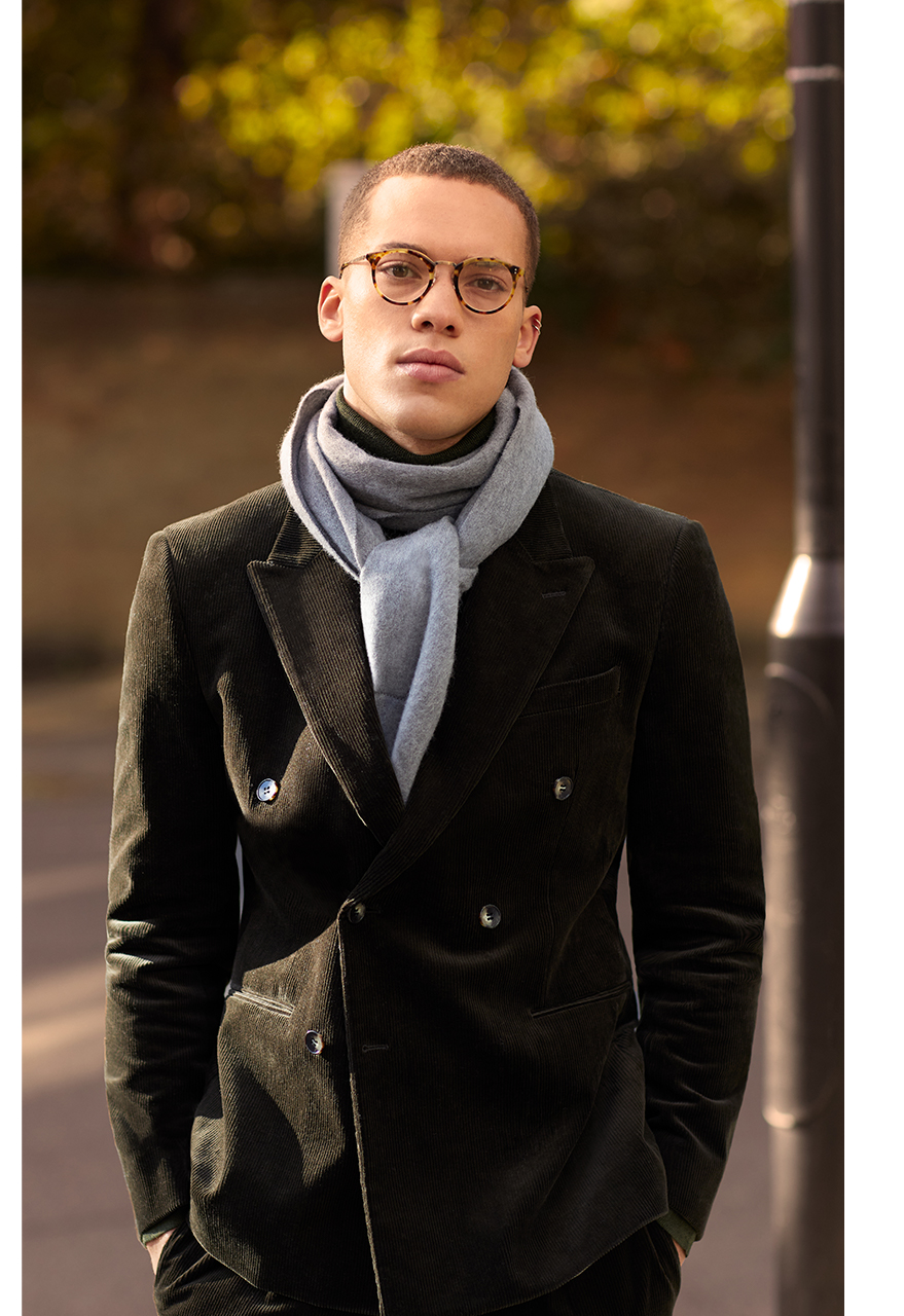 Man in glasses wearing a dark brown Moss Bros overcoat and a light grey scarf.
