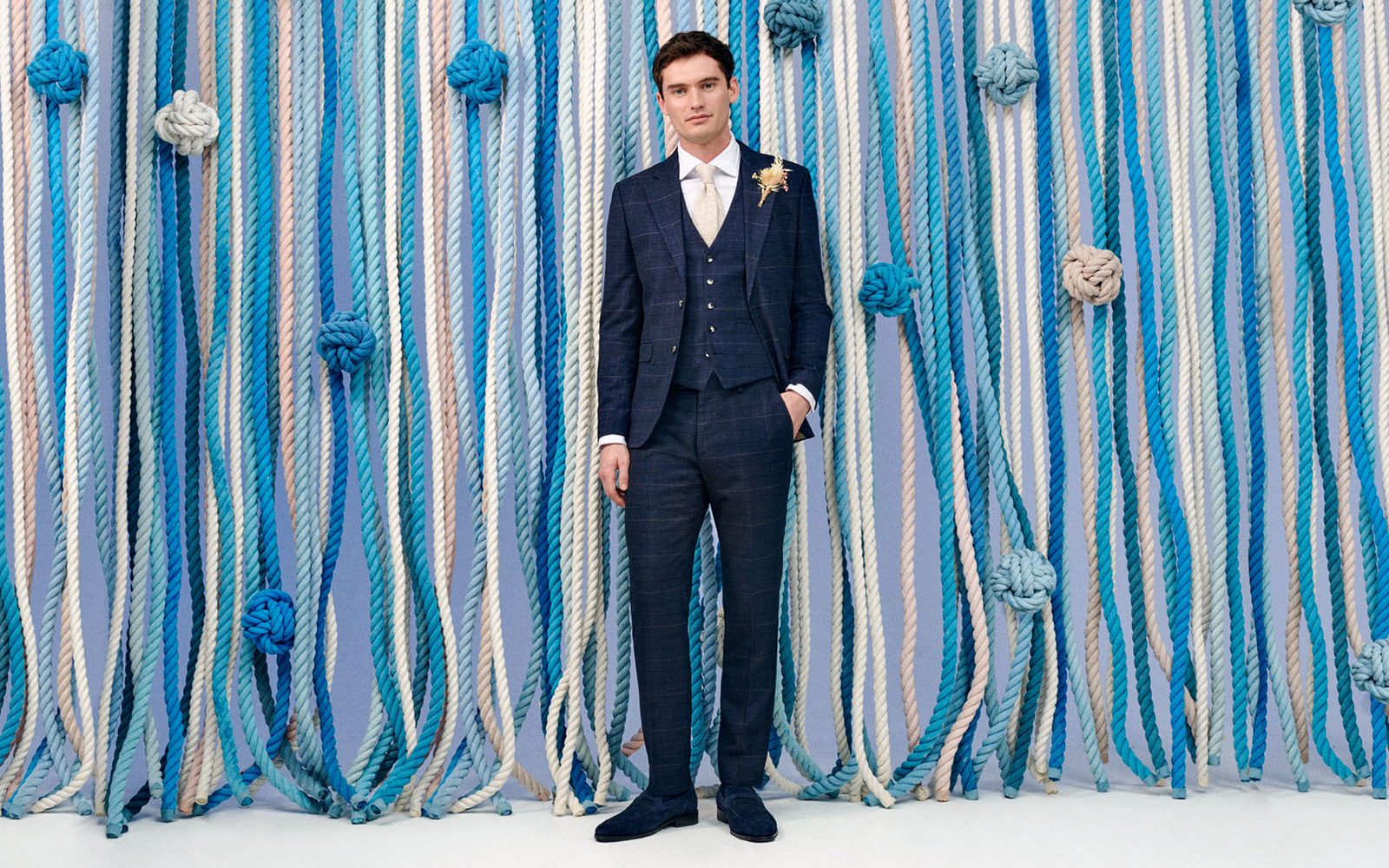 Groom in Moss Bros checked navy three piece suit and gold tie. A modern groom's outfit recommended for a groom opting for a contemporary look.