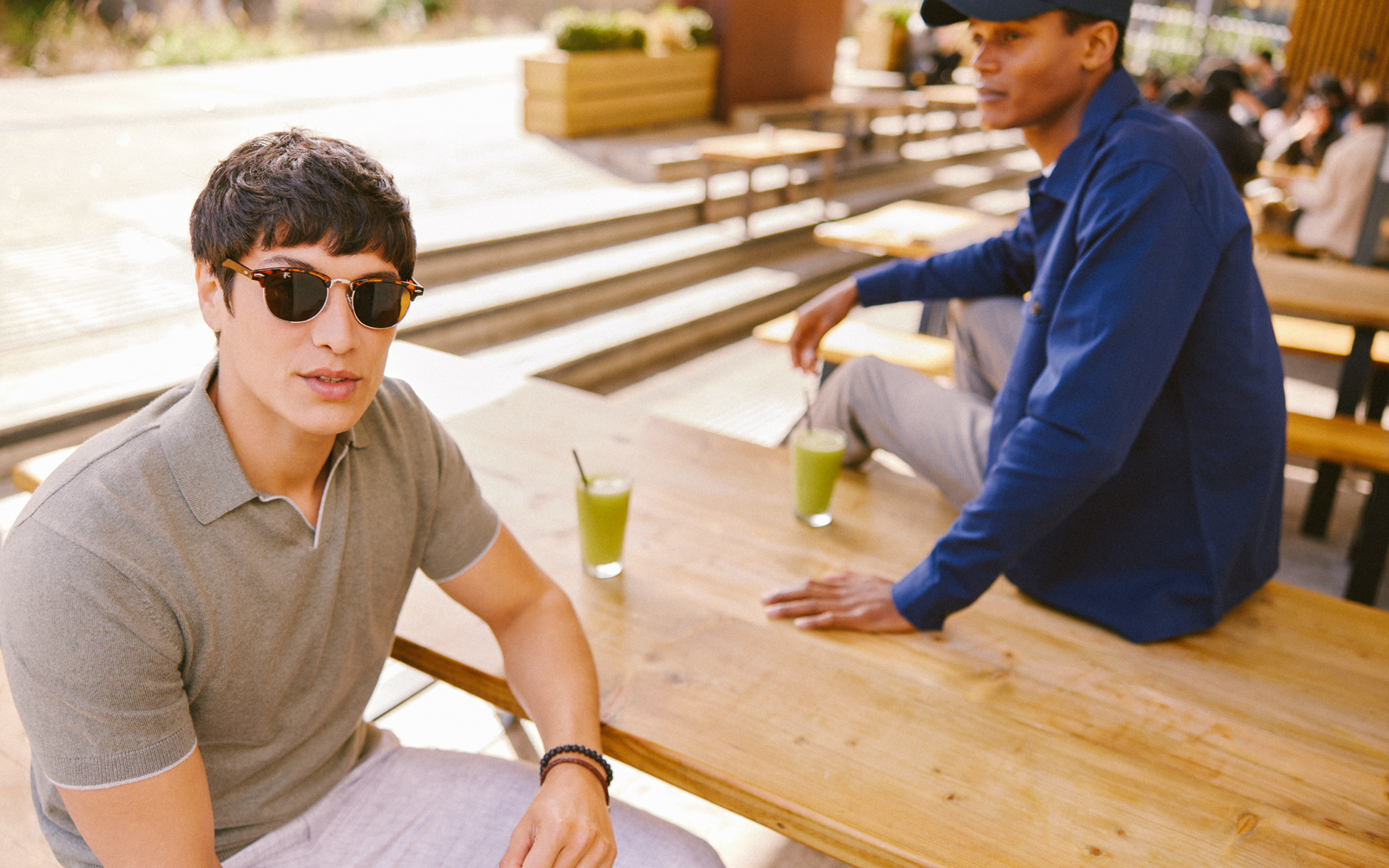 Two men sat with cocktails wearing grey and navy polo shirts and sunglasses.