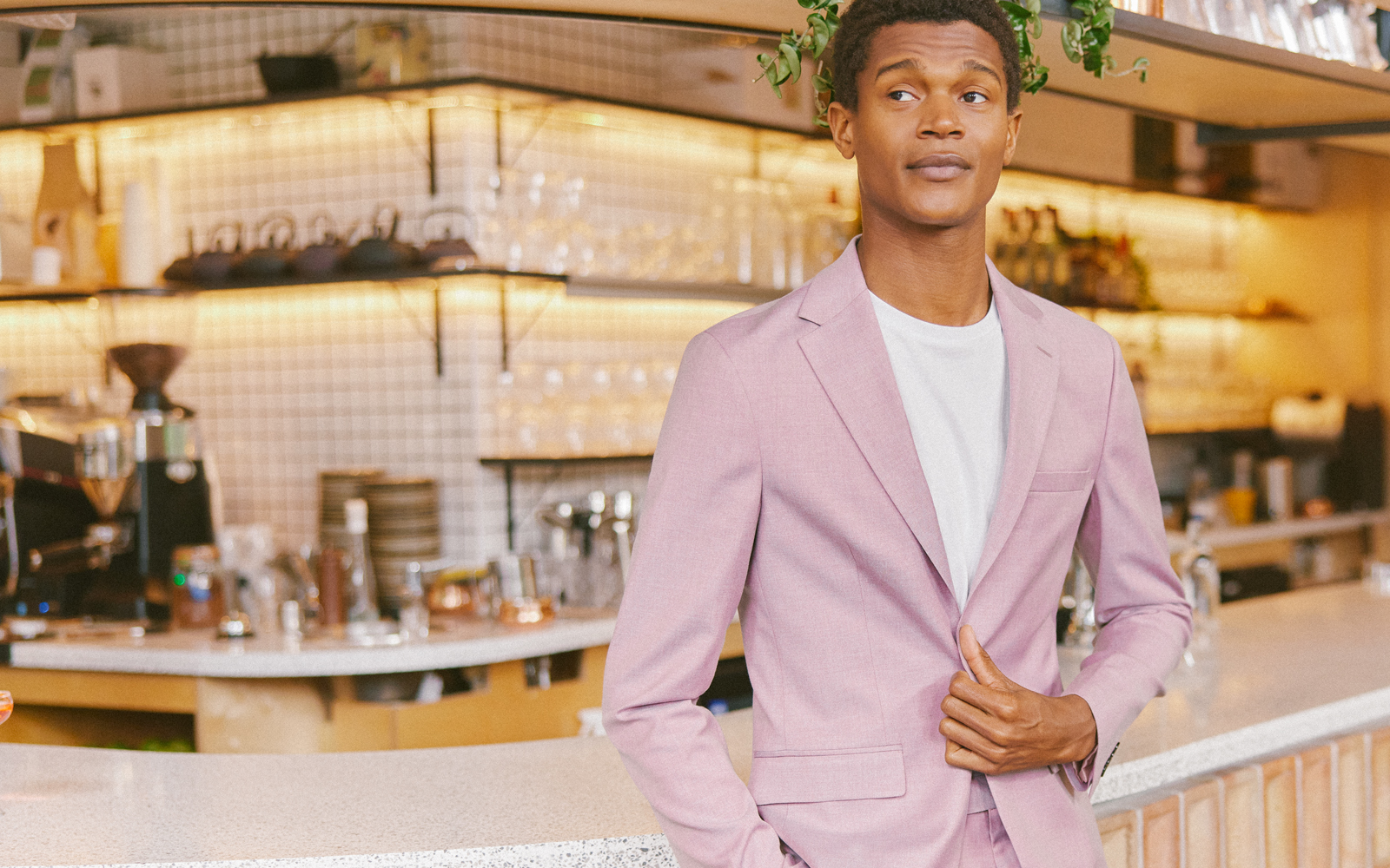 Man in white t shirt and light summer suit standing at a bar waiting for a date in summer.