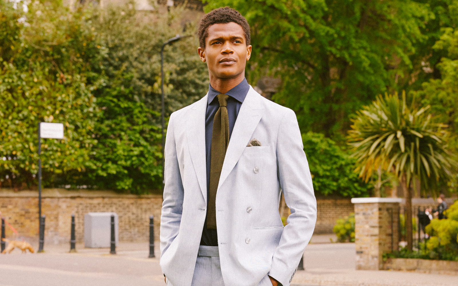 Man in white summer suit, green knitted tie and navy shirt looking into the distance.