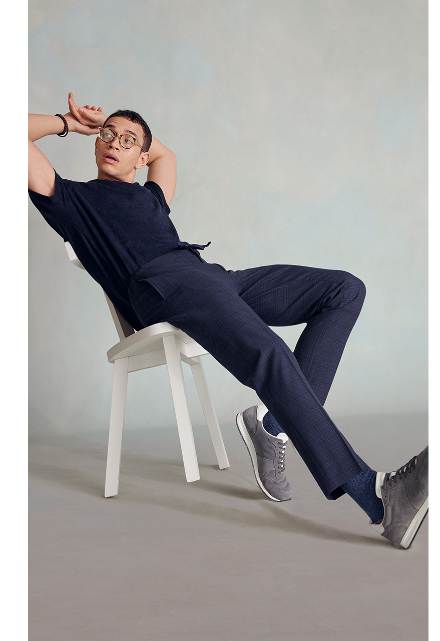 Man in casual work wear: a navy t shirt and checked navy trousers with grey trainers.