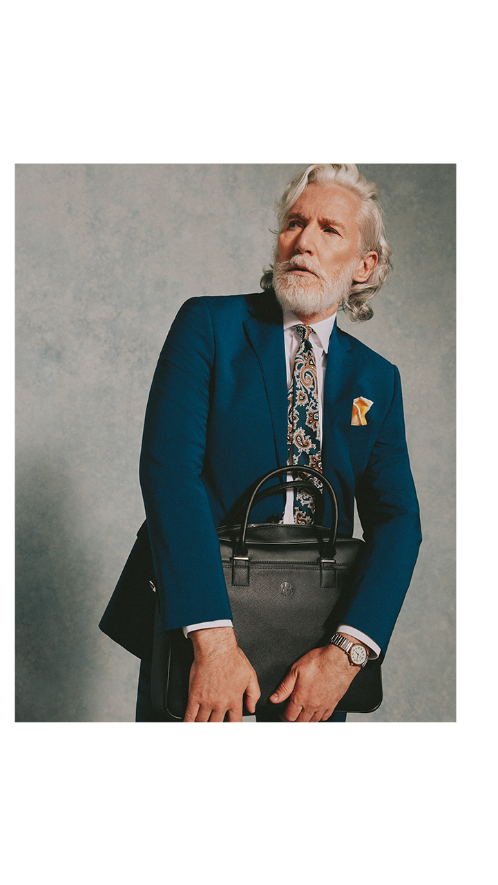 Professional going to work wearing a dark navy suit, floral tie and pocket square and holding a black leather bag.