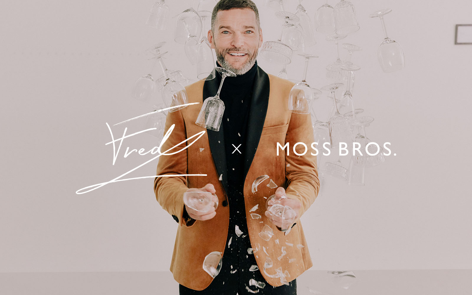 Fred Sirieix in tan Moss Bros jacket and black roll neck jumper with wine glasses falling around him.