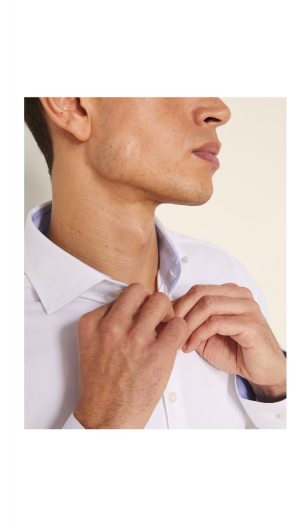 Man buttoning up a white oxford shirt. 