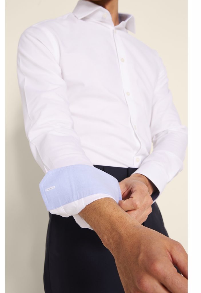 Man in white oxford shirt does up his cuffs. 