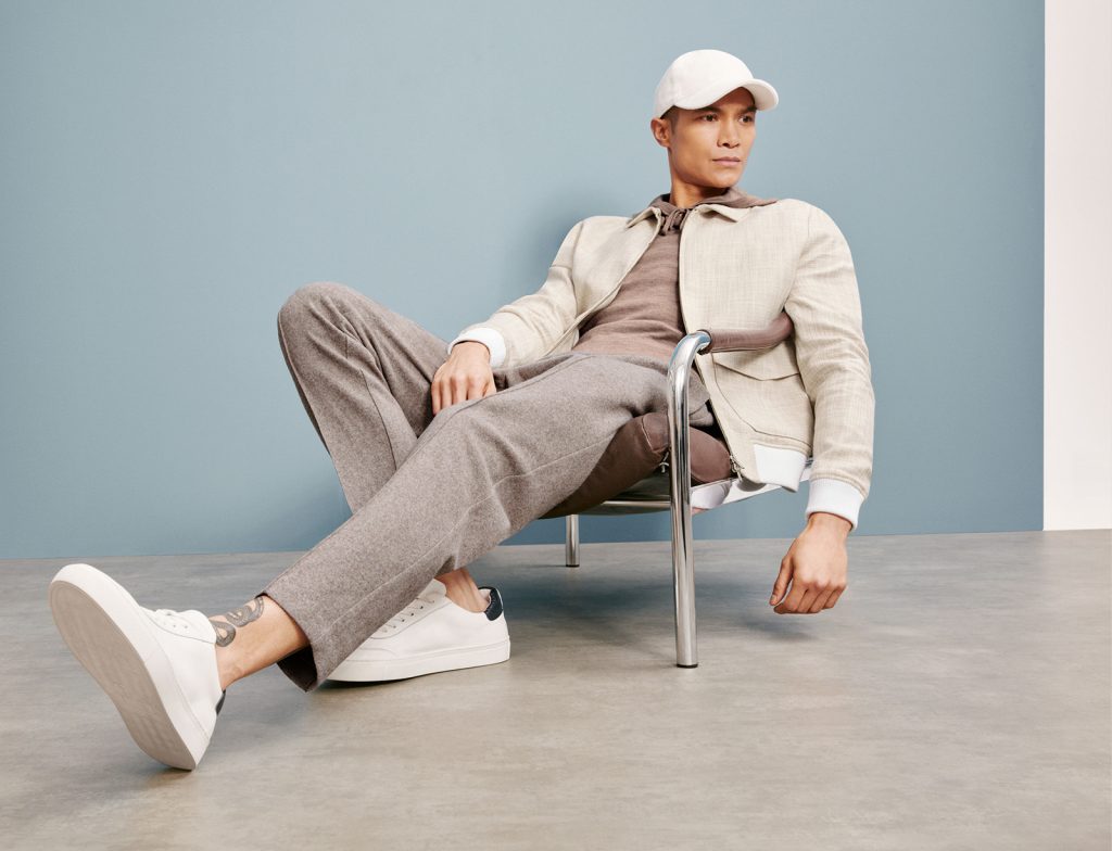 A man in holiday clothes dressed in cotton grey trousers, a cream shacket and a cream cap. 