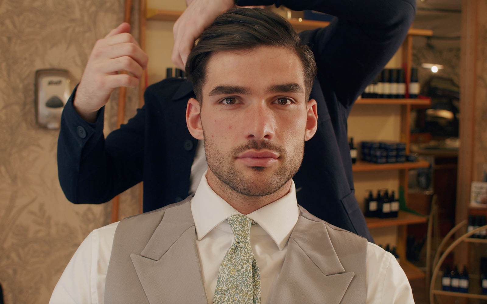 Man in a salon chair dressed for Ascot in a waistcoat, shirt and tie having his hair styled